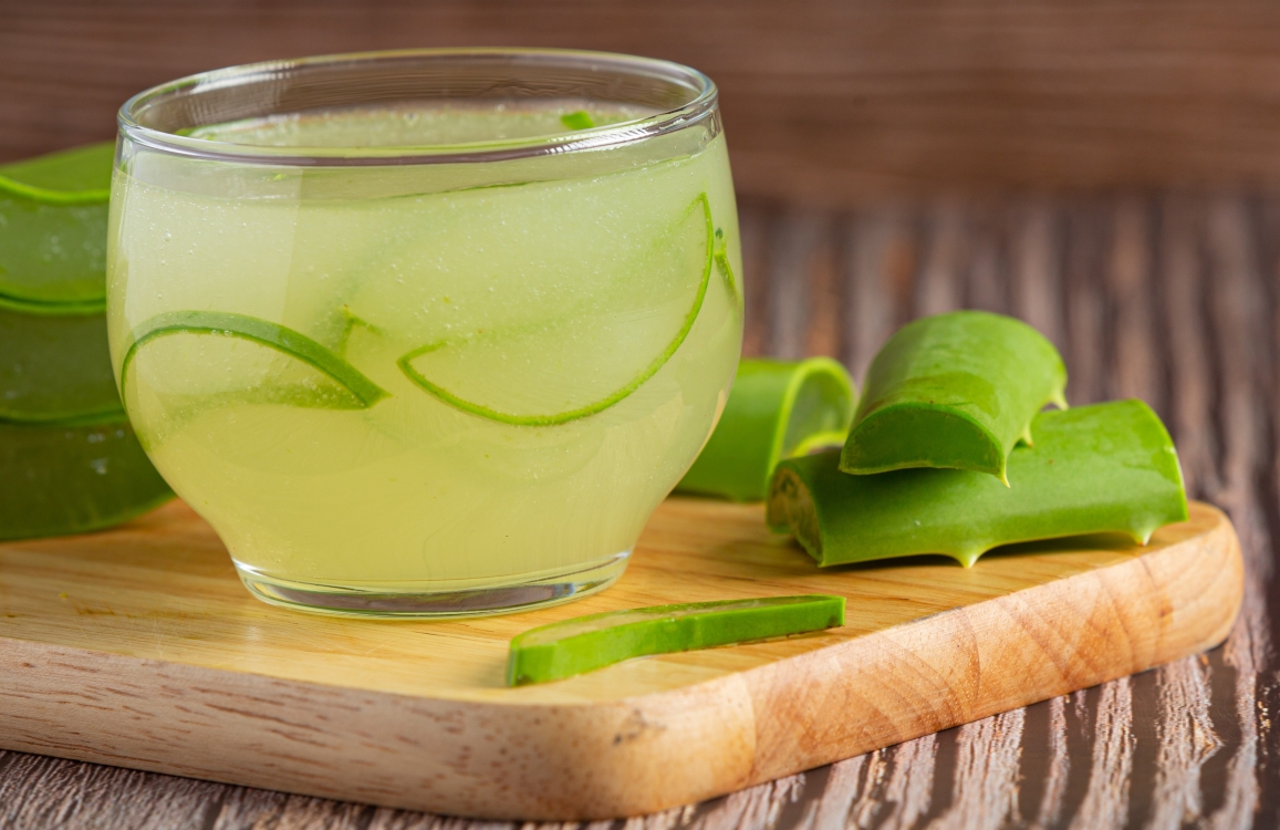 Sok aloe vere u čaši komadi lista na drvenoj dasci